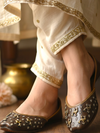 ThreadItStudio brown leather juttis with antique brass camel motifs and metallic studs worn with cream embroidered pants