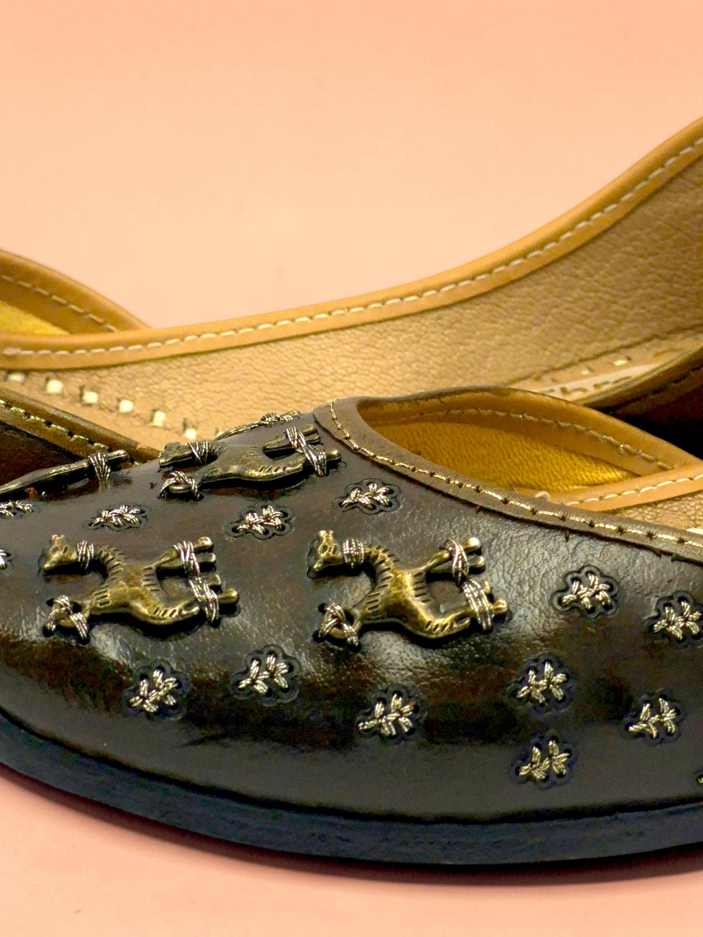 ThreadItStudio brown leather juttis with antique brass camel motifs and metallic studs on a soft pink background