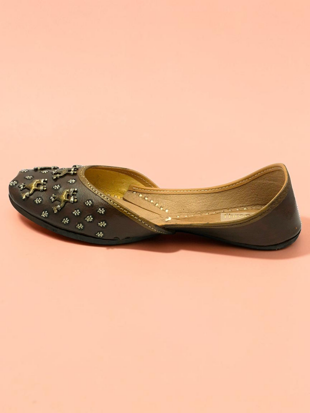ThreadItStudio brown leather juttis featuring antique brass camel motifs and metallic studs on a soft peach background