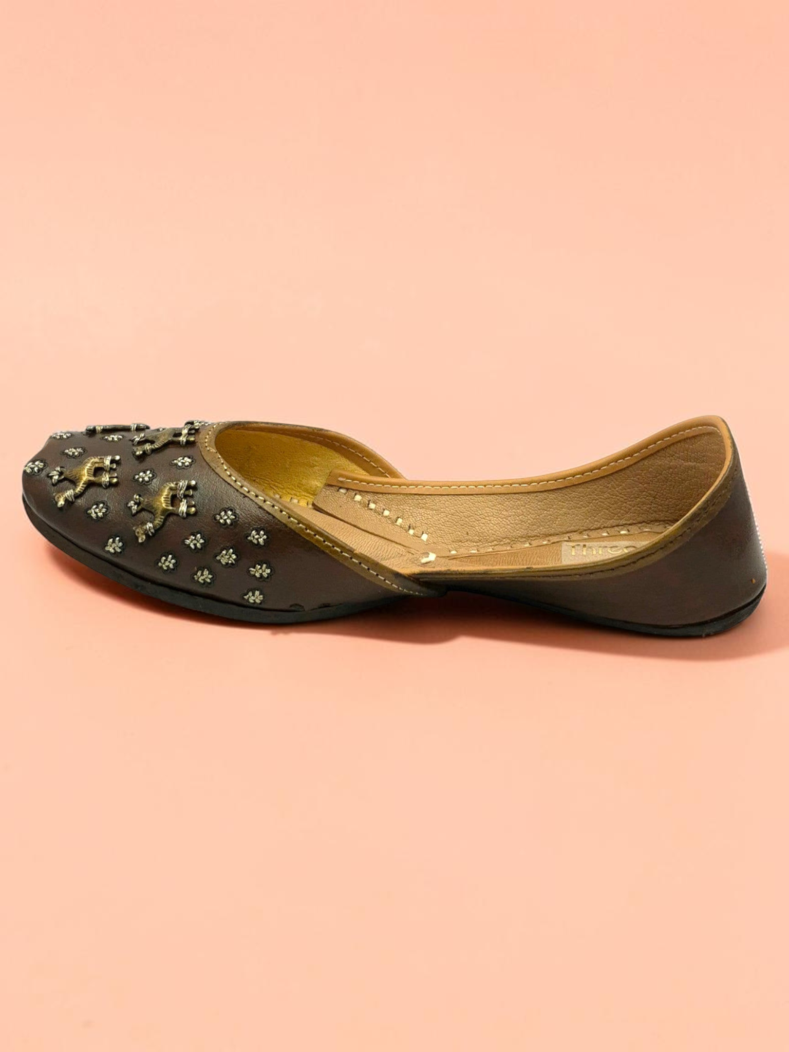 ThreadItStudio brown leather juttis featuring antique brass camel motifs and metallic studs on a soft peach background