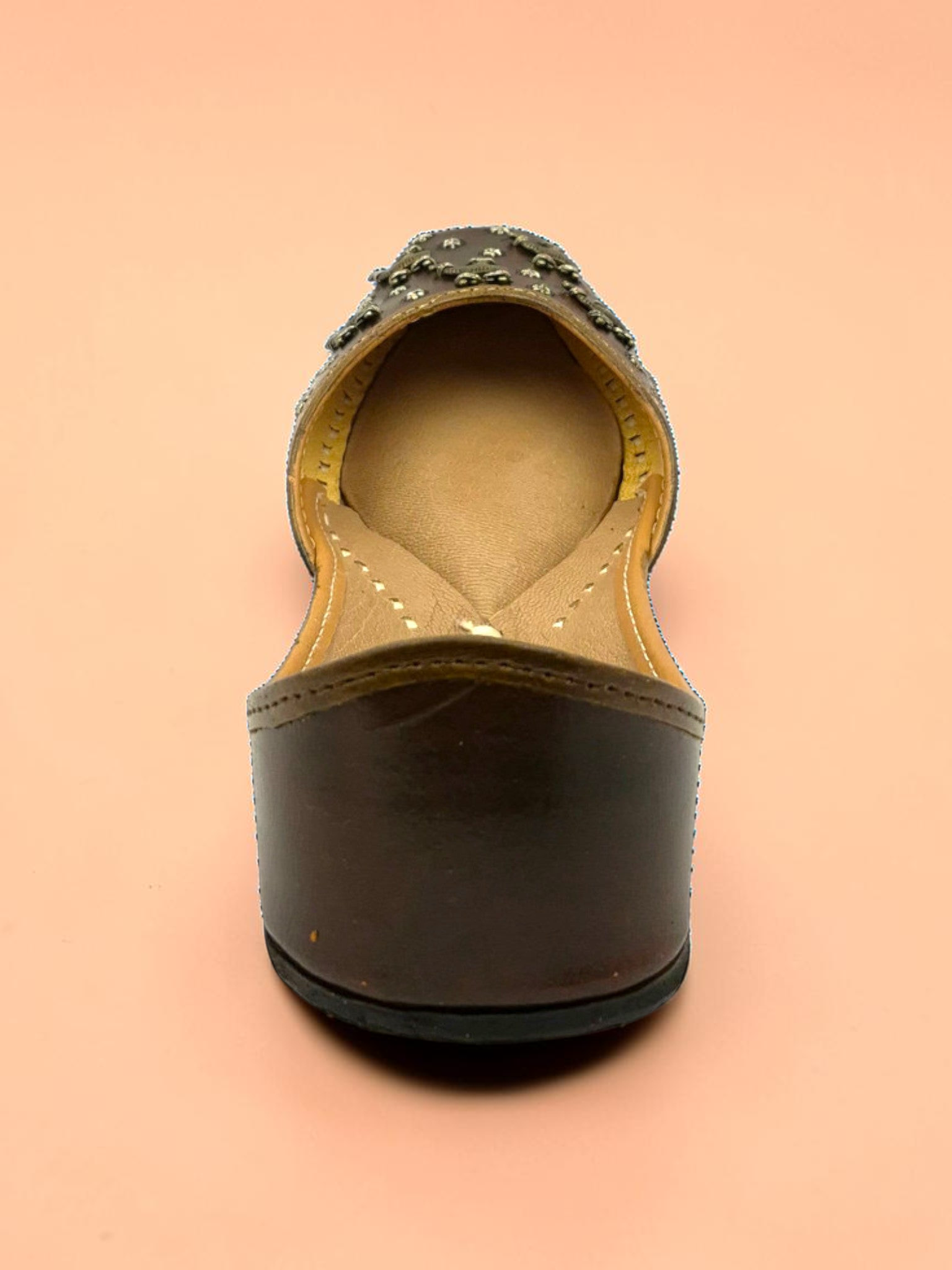 ThreadItStudio brown leather juttis featuring antique brass camel motifs and metallic studs on a peach background