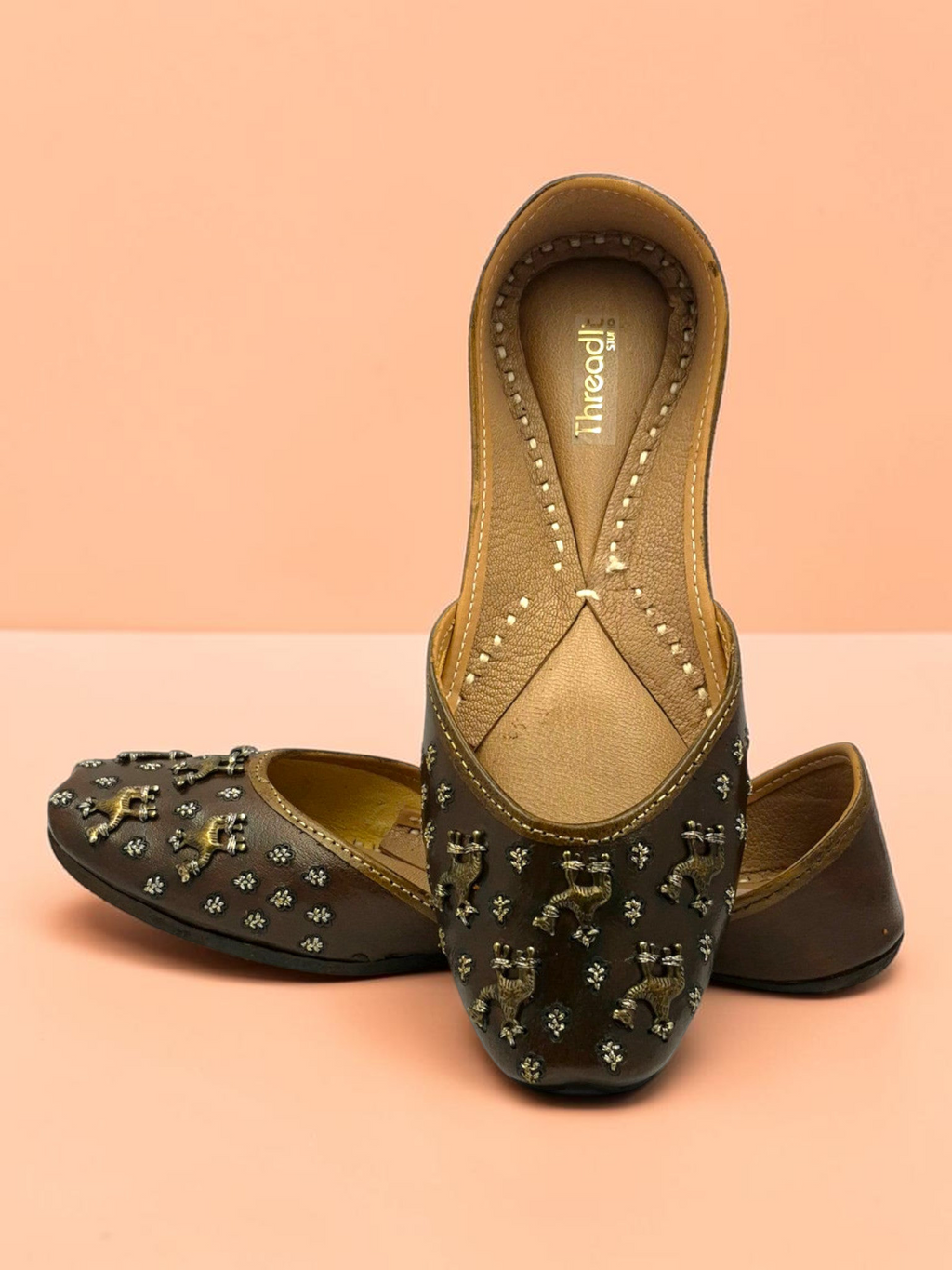 ThreadItStudio brown leather juttis featuring antique brass camel motifs and delicate metallic stud embellishments.