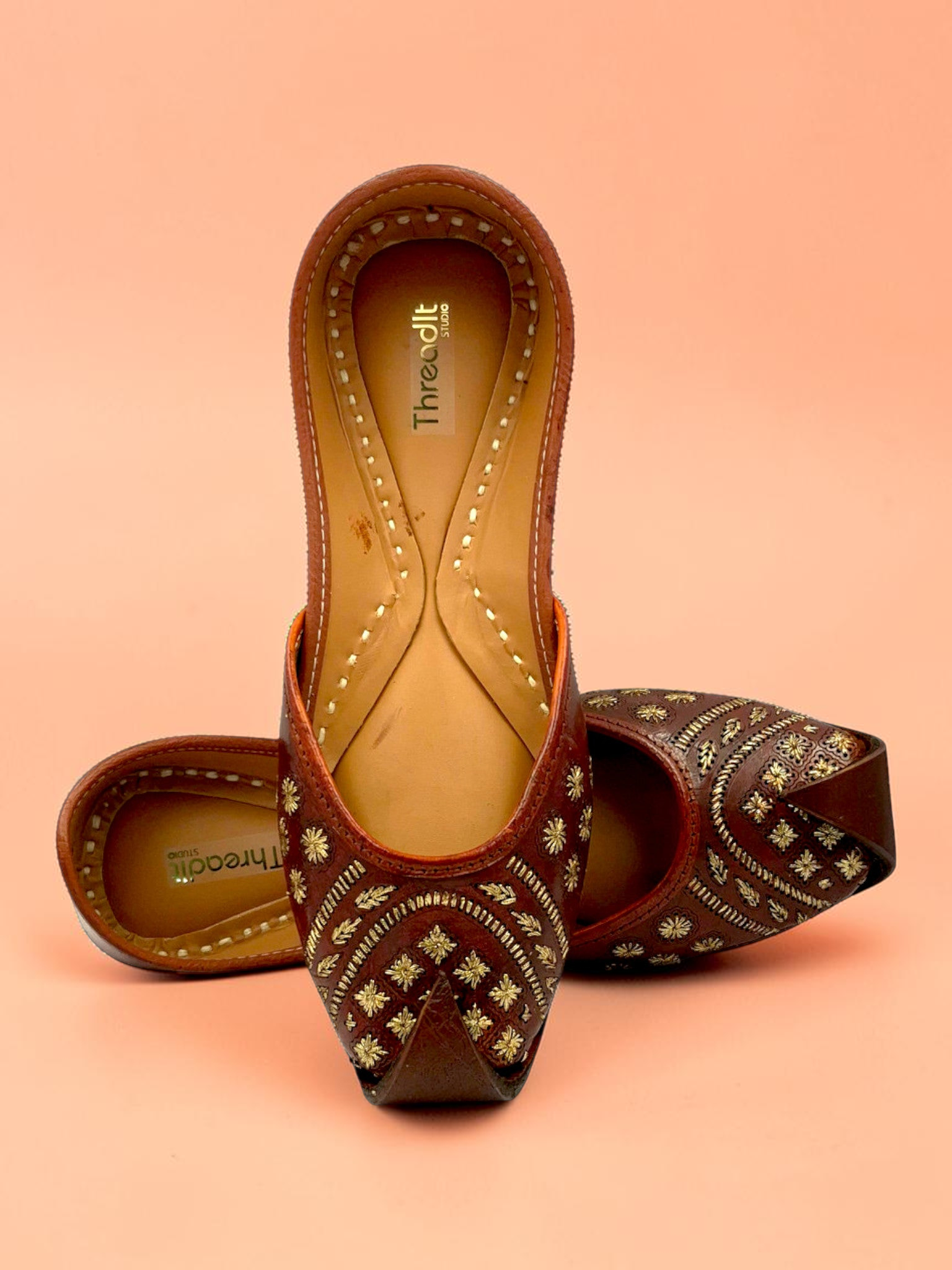 ThreadItStudio brown leather juttis with intricate gold floral embroidery and traditional curved toe design.