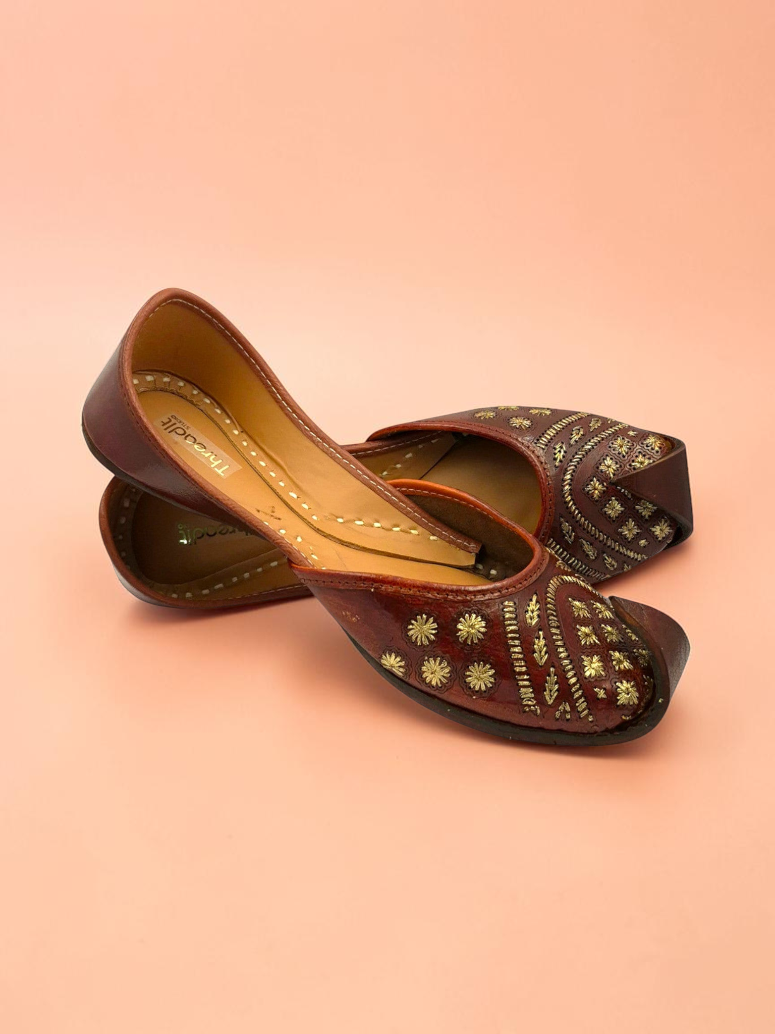 ThreadItStudio brown leather juttis with gold floral embroidery and traditional curved toe design for ethnic wear.