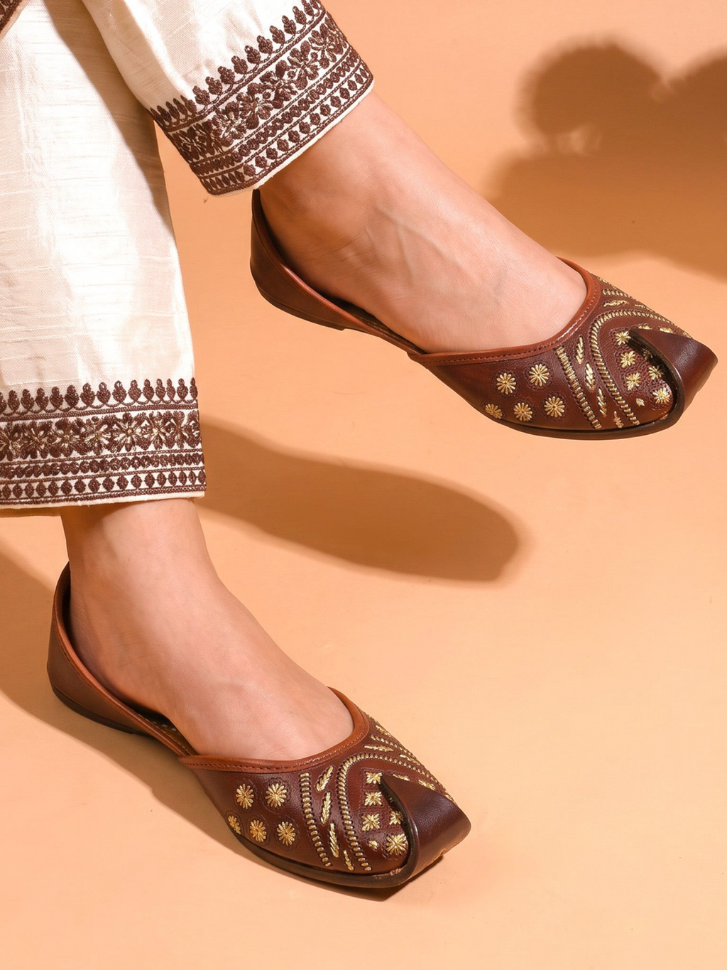 ThreadItStudio brown leather juttis with gold floral embroidery and geometric stitching worn with white trousers