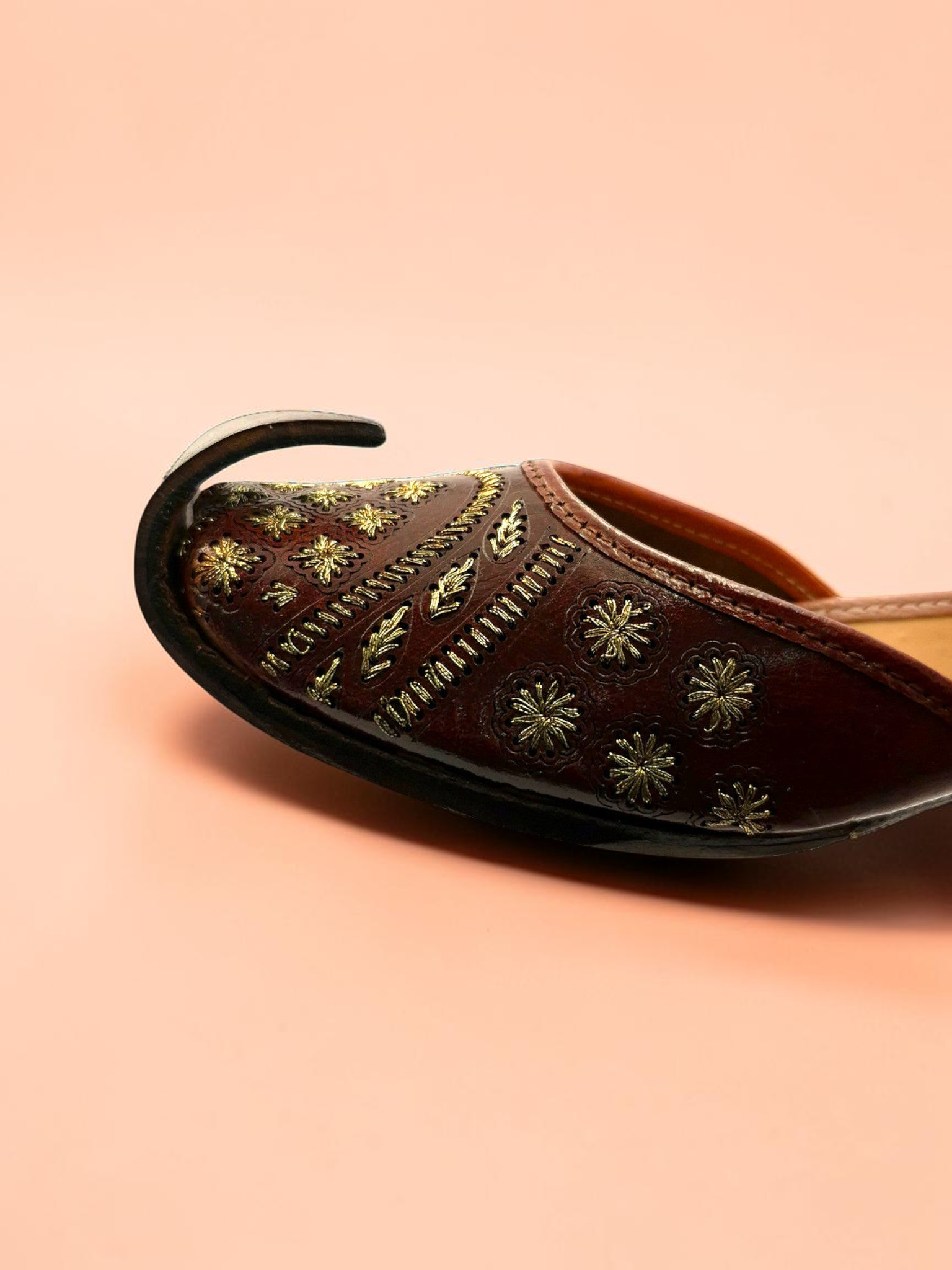ThreadItStudio brown leather jutti with intricate gold floral embroidery and a classic curved toe on a peach background