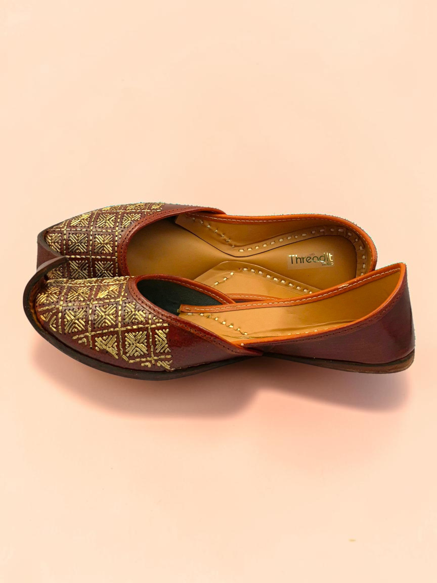 ThreadItStudio Rang Punjab brown leather juttis with intricate gold-thread grid embroidery and curved toe design.