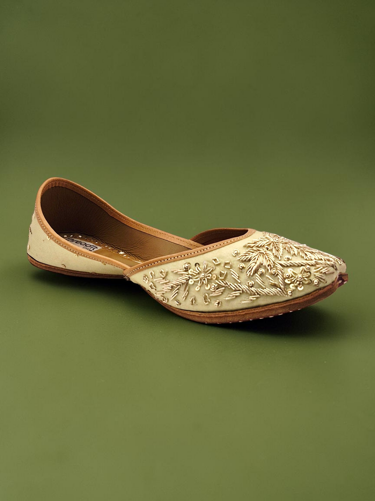ThreadItStudio handcrafted jutti with intricate golden embroidery and beadwork on a cream base for festive wear.