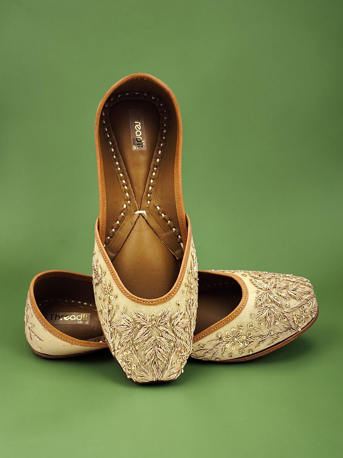 ThreadItStudio handcrafted jutti with intricate golden embroidery on a cream base for festive occasions.