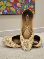 ThreadItStudio handcrafted beige jutti with intricate golden peacock embroidery, perfect for weddings and festivals.