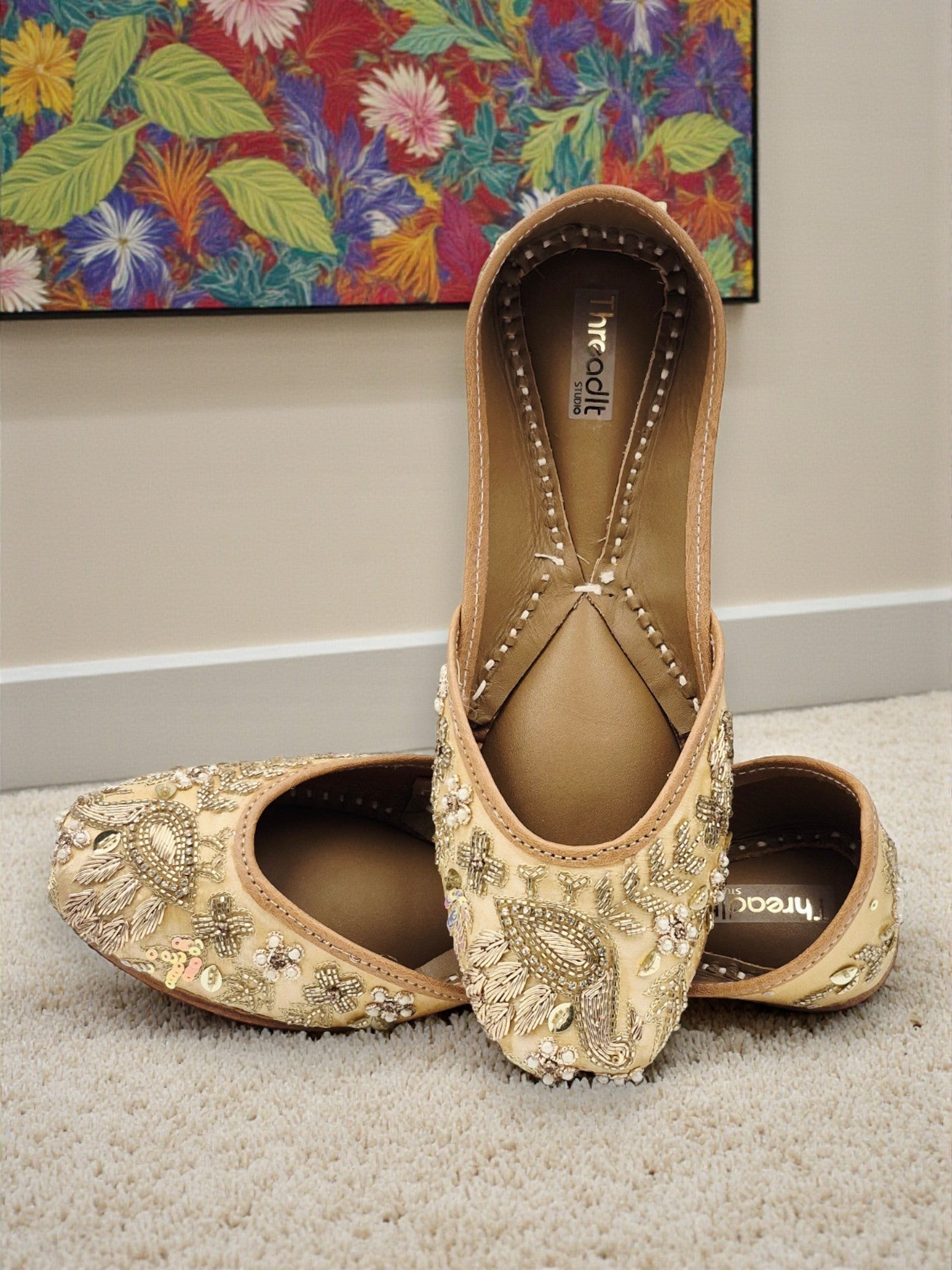 ThreadItStudio handcrafted beige jutti with intricate golden peacock embroidery, perfect for weddings and festivals.