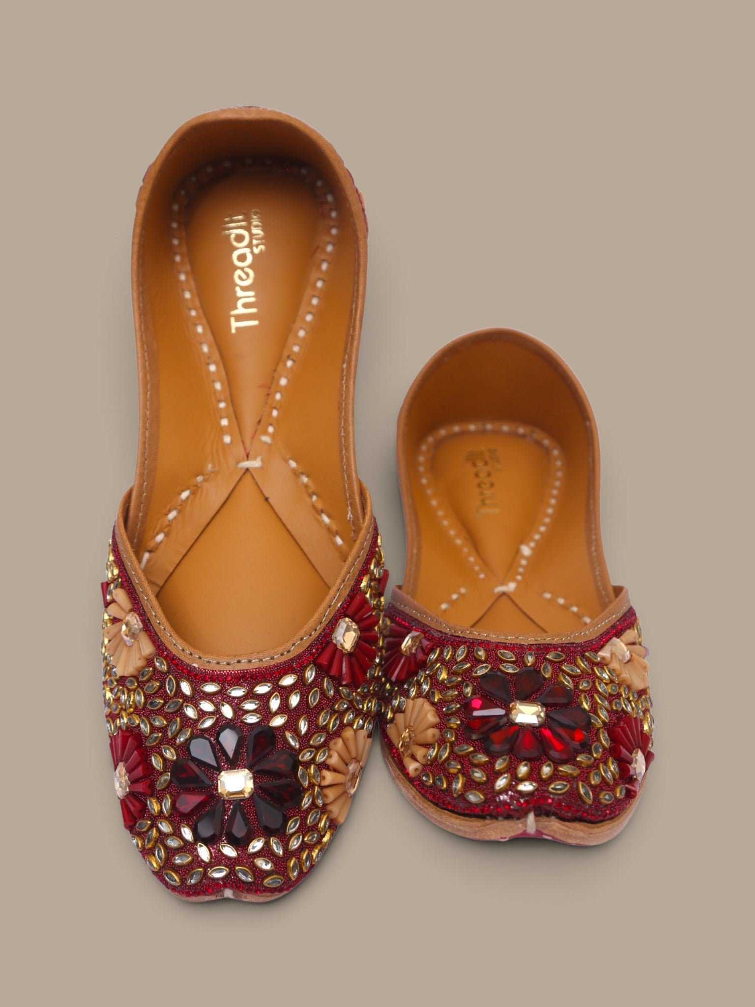 ThreadItStudio handcrafted ethnic jutti featuring intricate red and gold kundan beadwork on a brown leather base.