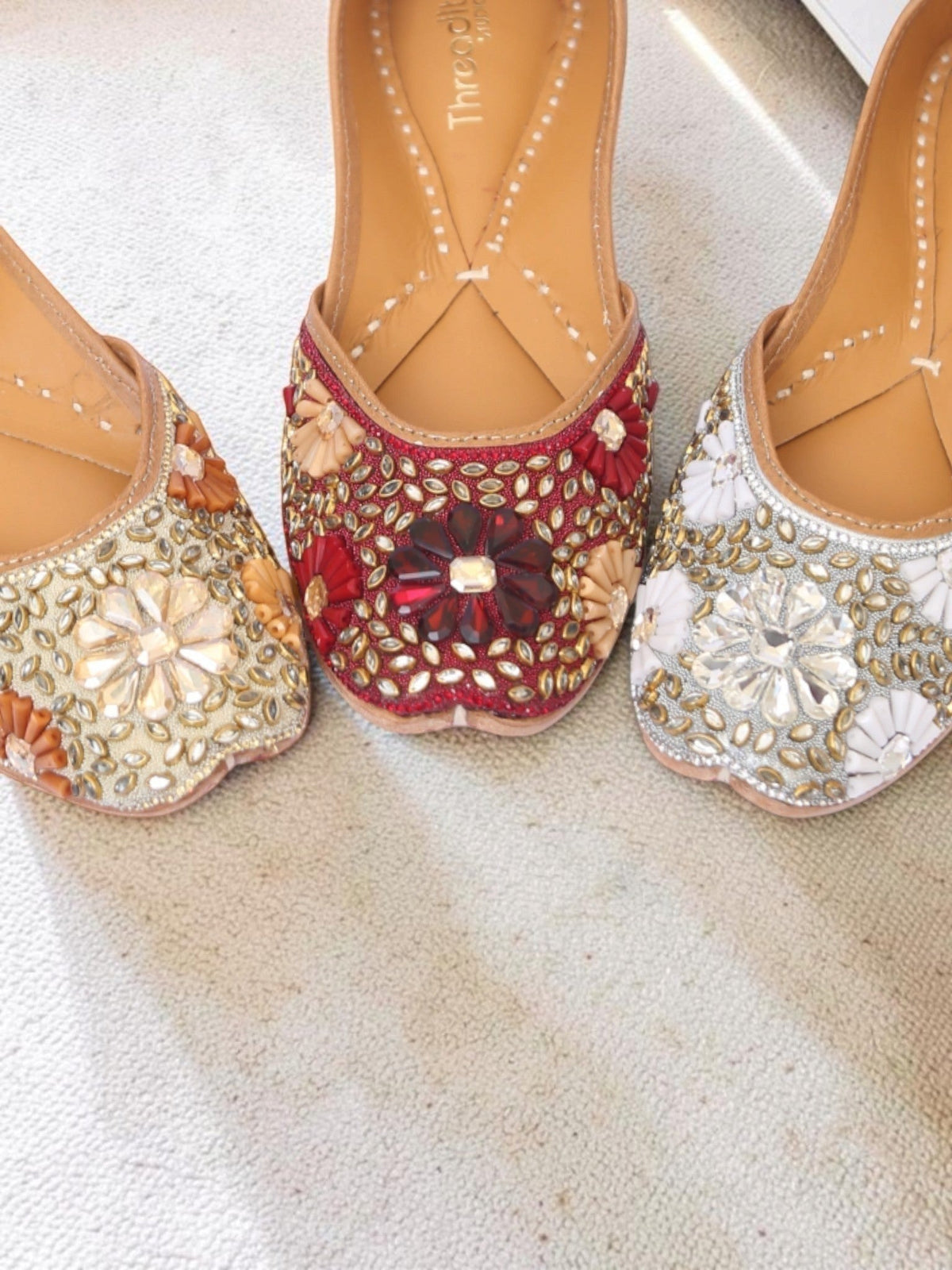 ThreadItStudio handcrafted ethnic juttis featuring intricate kundan beadwork in red, gold, and silver floral patterns.