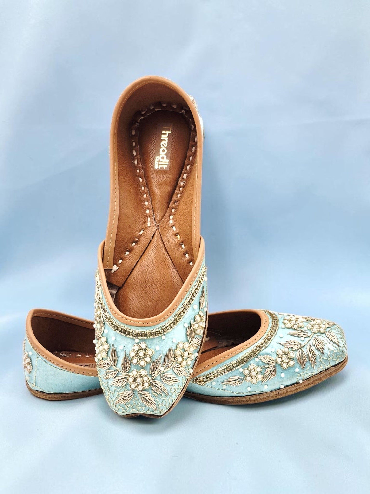 ThreadItStudio handcrafted sky blue ethnic jutti with intricate floral embroidery and pearl detailing on a blue base.