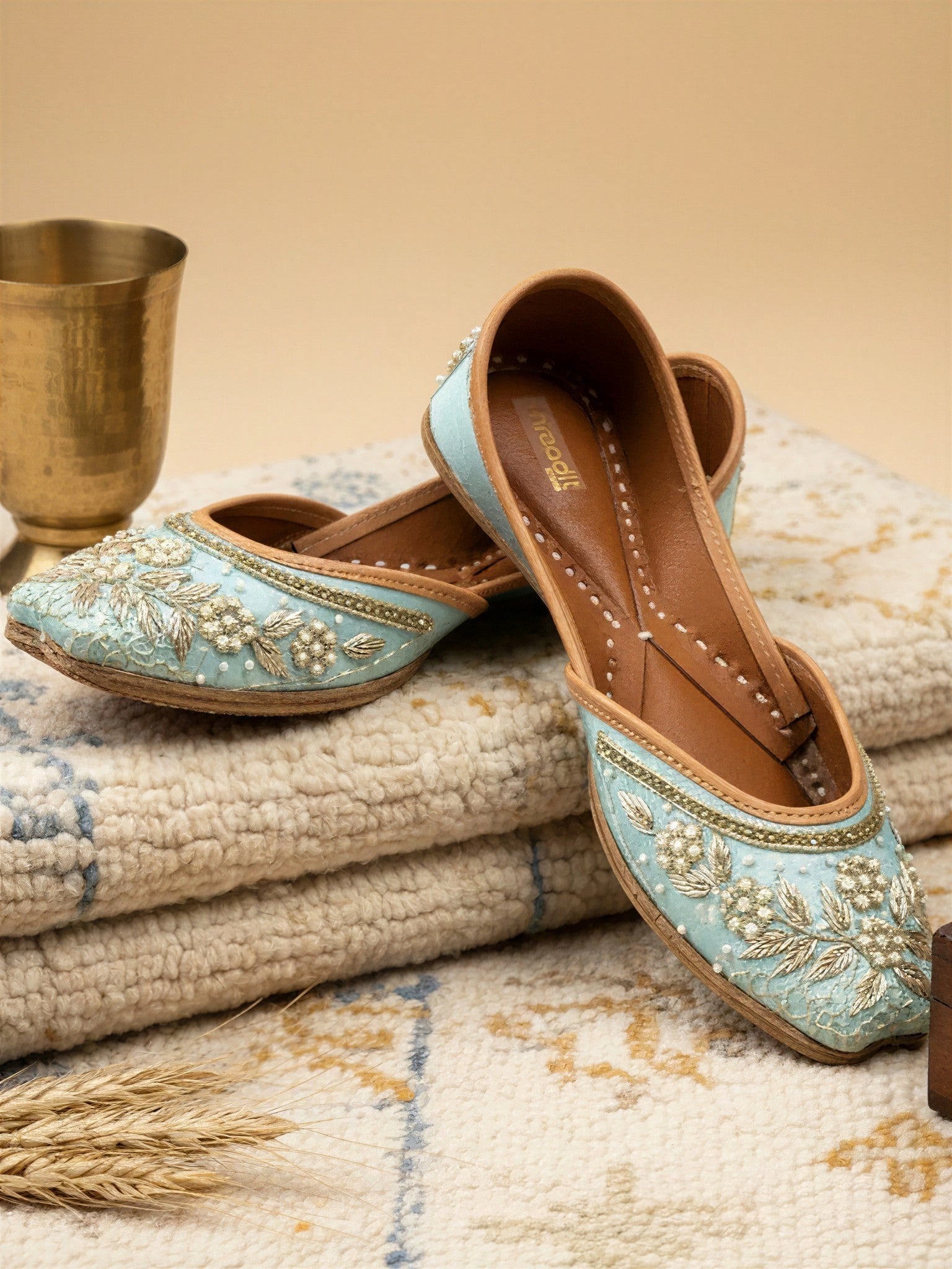 ThreadItStudio handcrafted sky blue ethnic jutti with intricate gold embroidery and pearl detailing on a textured rug.