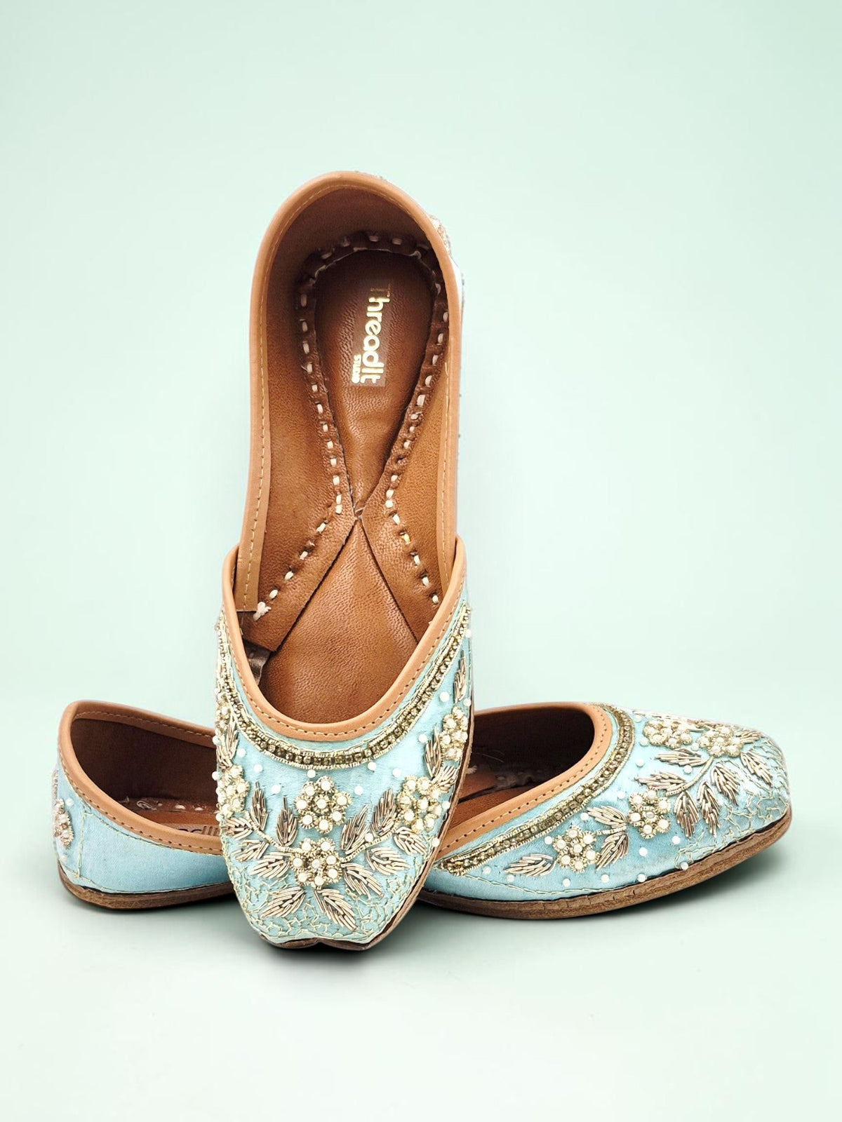 ThreadItStudio sky blue handcrafted ethnic jutti with intricate floral embroidery and pearl detailing on a blue background