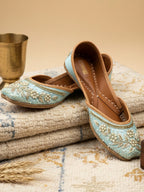 ThreadItStudio handcrafted sky blue ethnic jutti with intricate gold embroidery and pearl detailing on a textured rug.