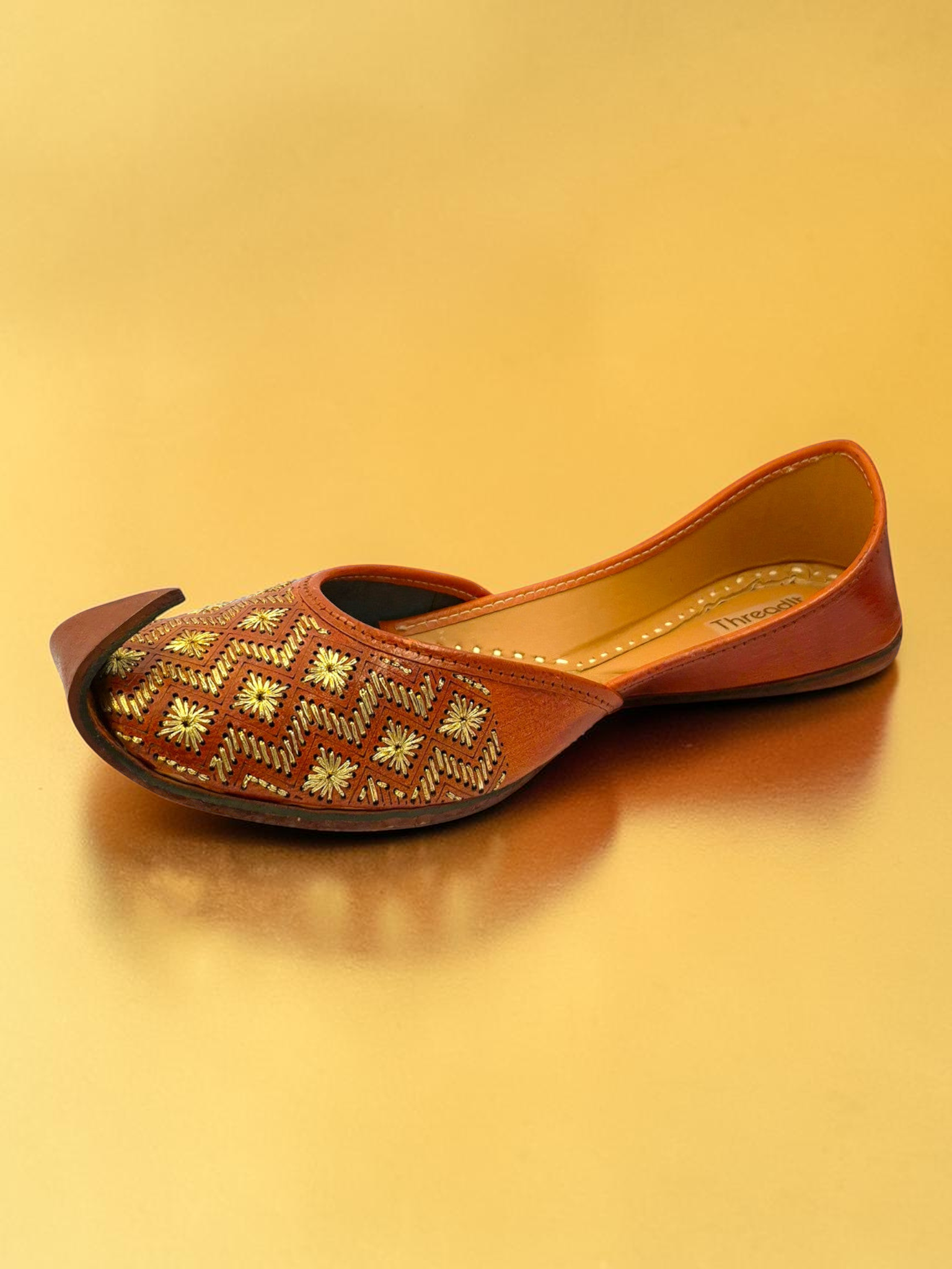 ThreadItStudio tan leather jutti with gold geometric embroidery and floral motifs on a metallic gold background.