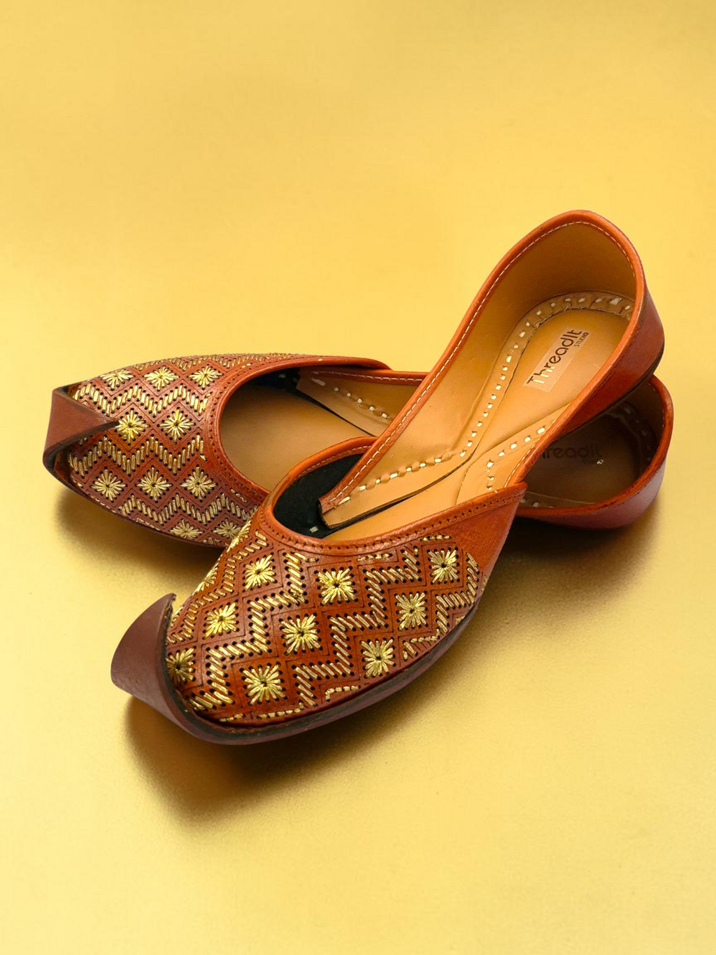 ThreadItStudio tan leather juttis with gold chevron embroidery and starburst floral motifs on a gold background