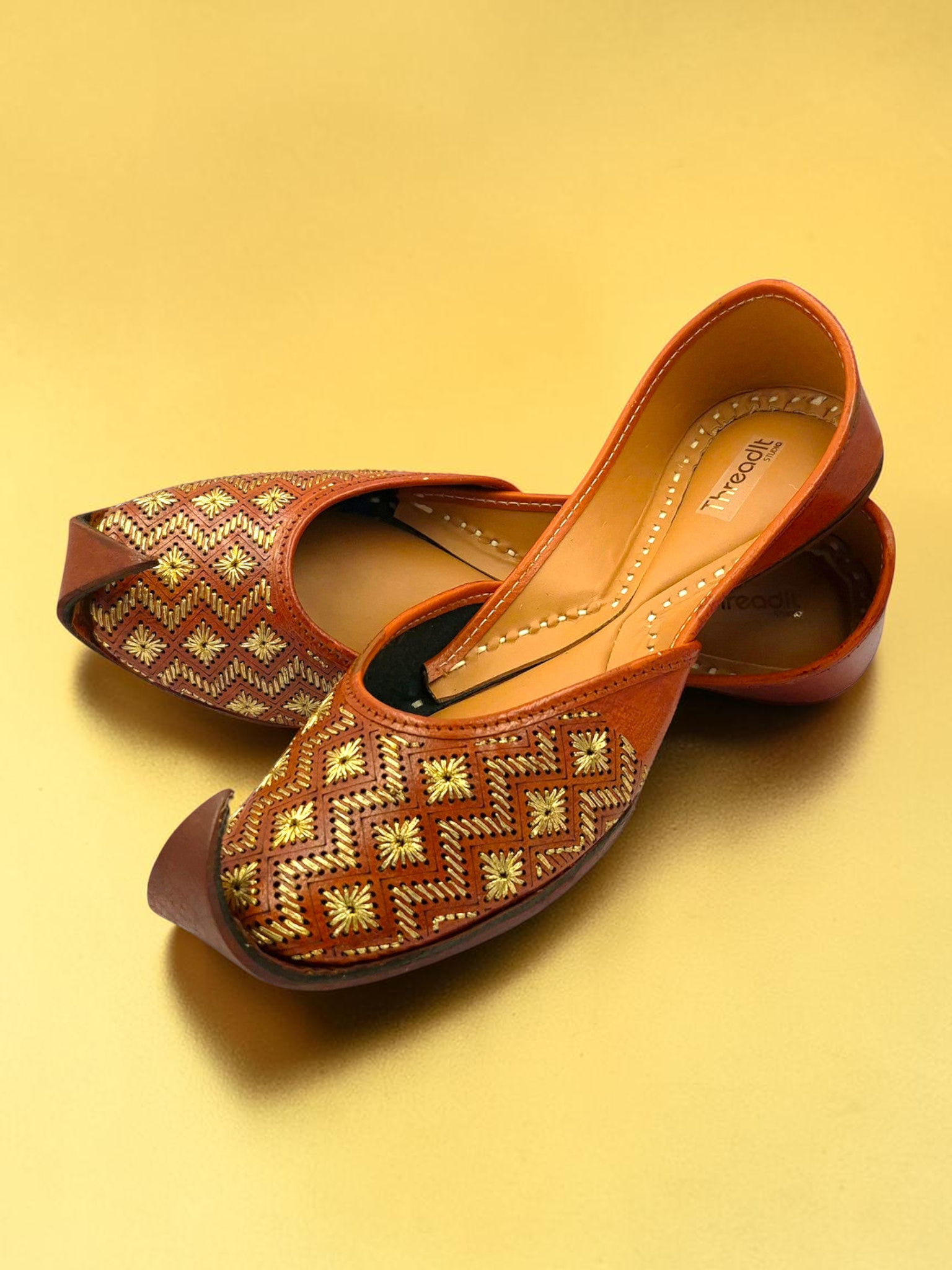 ThreadItStudio tan leather juttis with gold chevron embroidery and starburst floral motifs on a gold background