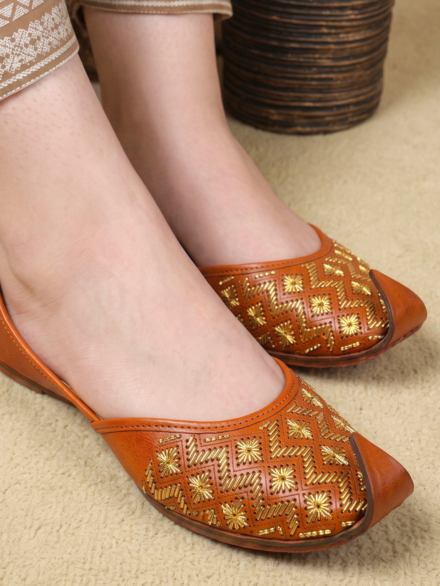 ThreadItStudio tan-brown leather juttis with gold-thread geometric chevron embroidery and starburst floral motifs